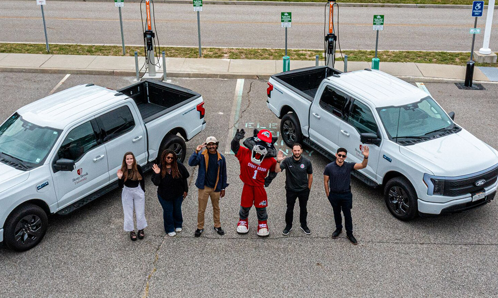 Sustainability students, staff, and Wolfie waving to camera next to new EV charging stations