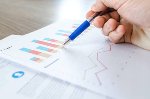 Papers with charts and graphs and a person holding a pen