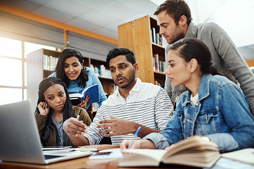 Student in a library collaborating and gathered around a laptop