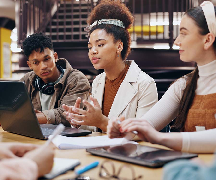Three students at a table in front of a laptop discussing
