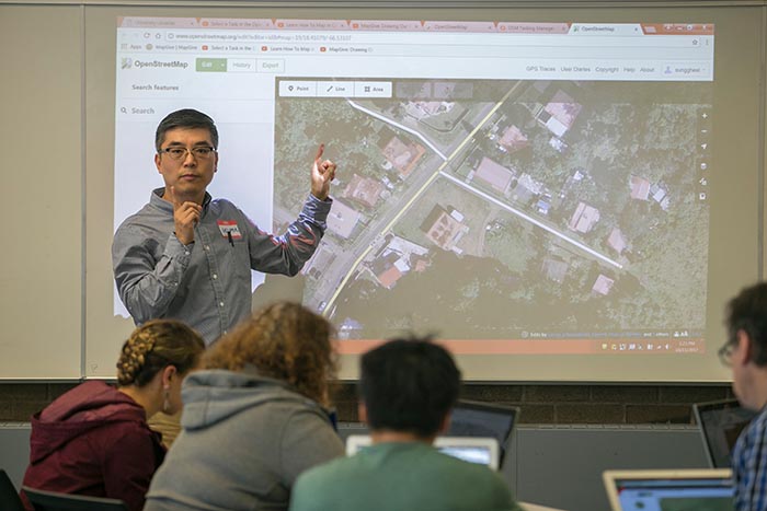 Gil Jang stands in front of a projector screen and instructs a GIS class