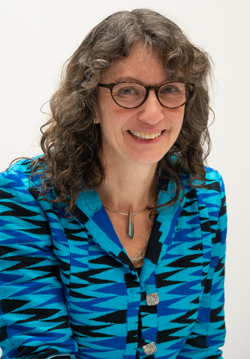 Alison Phipps headshot, has wavy hair, glasses and blue patterned shirt