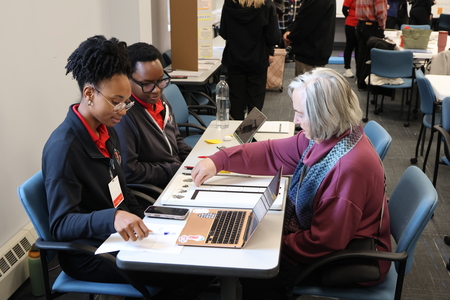 Two students and an older adult working together at a table with a laptop