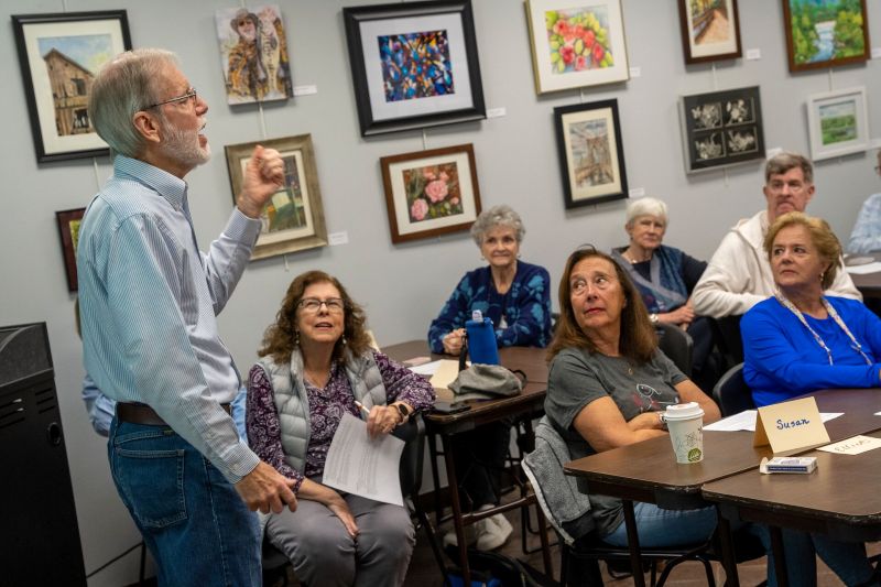 An OLLI member leading a discussion for a small group of seated adult learners listening attentively.