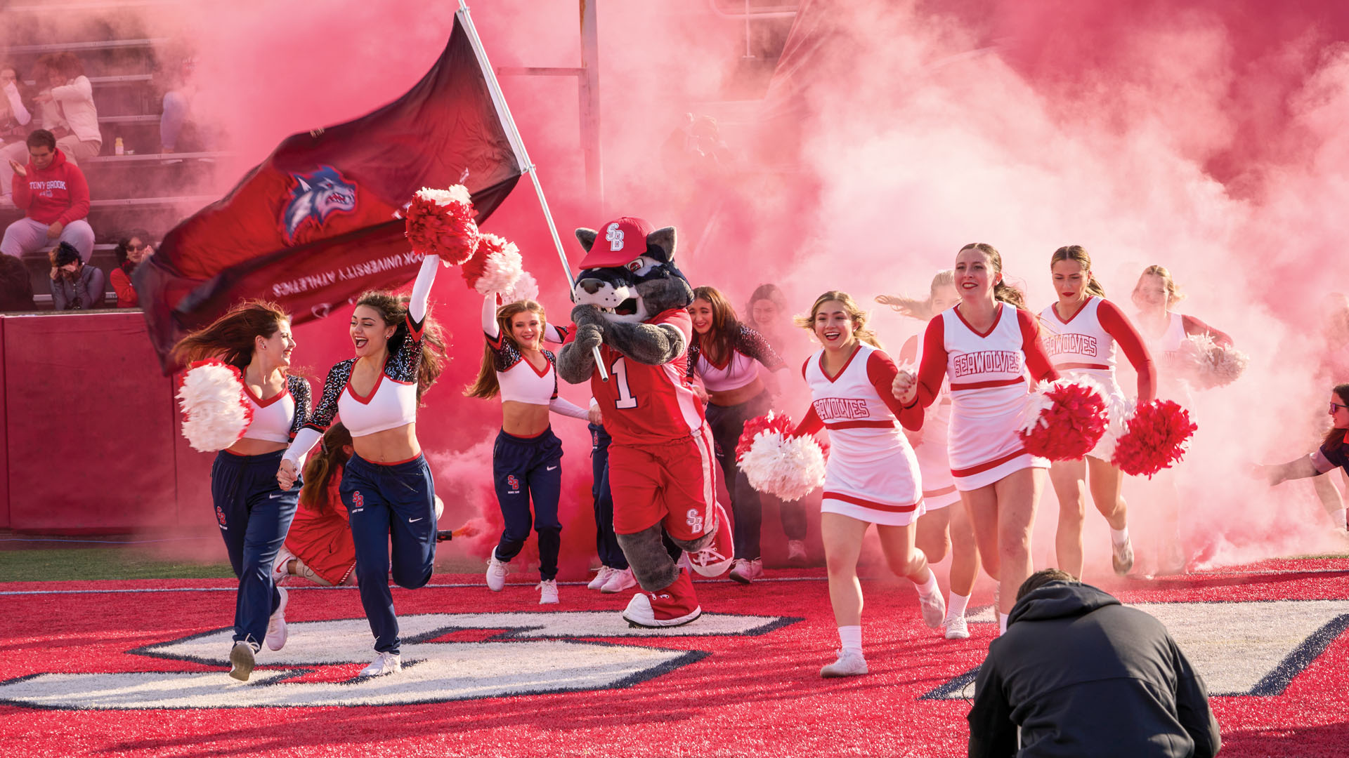 Woflie and students running through Stony Brook Stadium