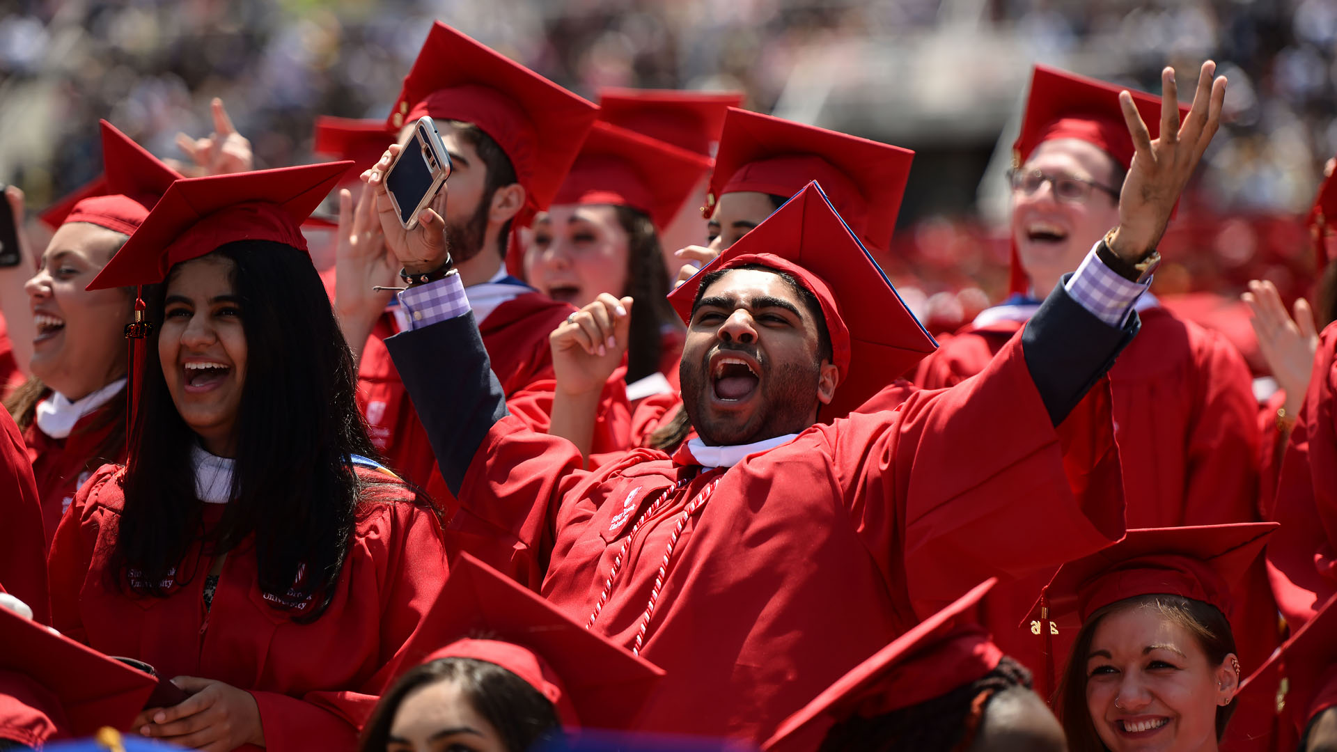 Graduates in red gowns clapping in a hall.
