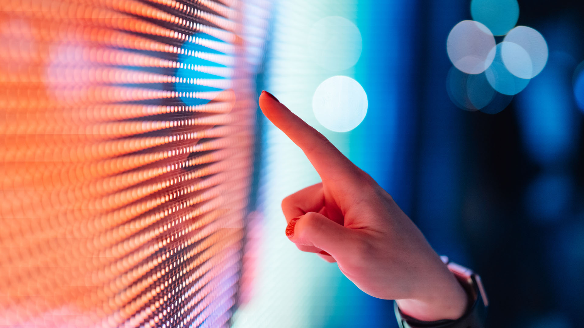 A hand with a finger pointing at a multicolor light display.