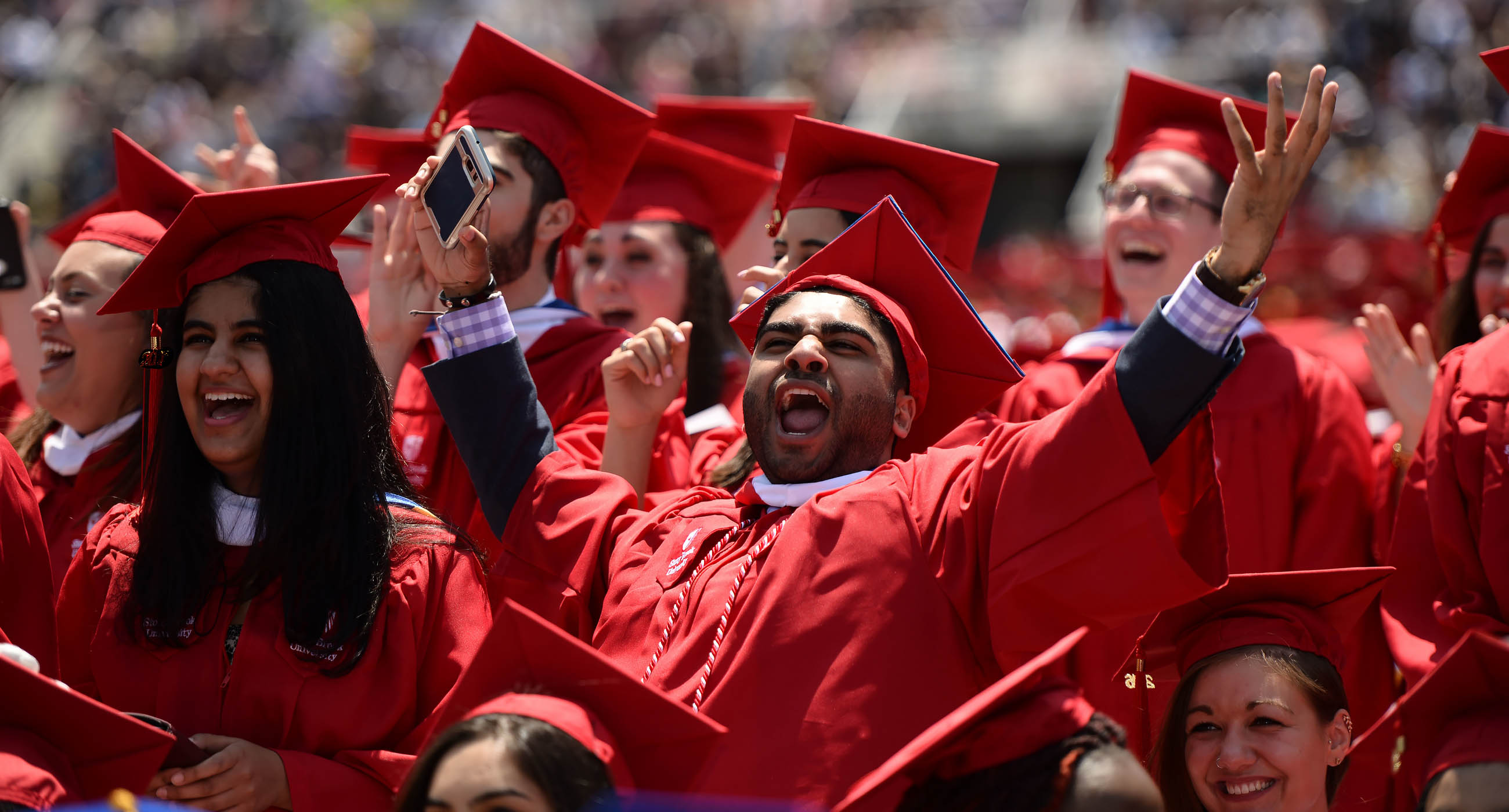 Stony Brook students cheering in graduation caps and gowns