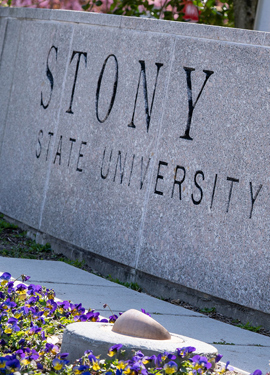 Stone sign reading “Stony Brook State University” with flowers in the foreground.