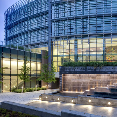 Glass-fronted Simons Center for Geometry and Physics lit up at dusk.