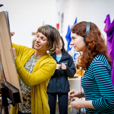 An art teacher reviewing a student's work on a large canvas