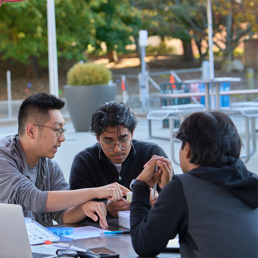 Three students studying outdoors at table