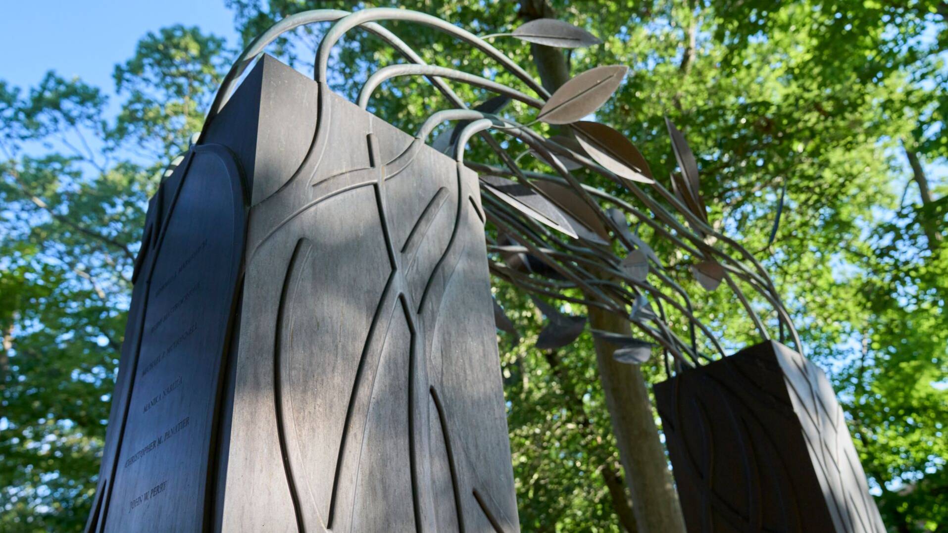 Photo of a September 11th memorial sculpture at SBU: Two metal towers with intertwined leaves. Blue sky and trees visible above the sculpture.
