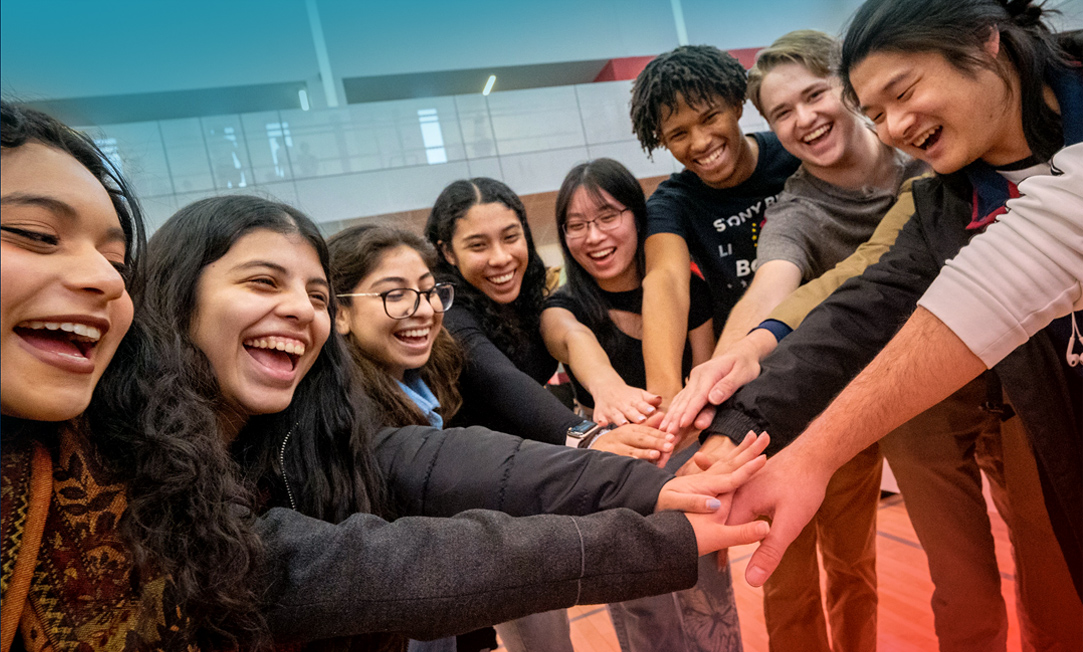 Students in a circle with their hands on top of eachother