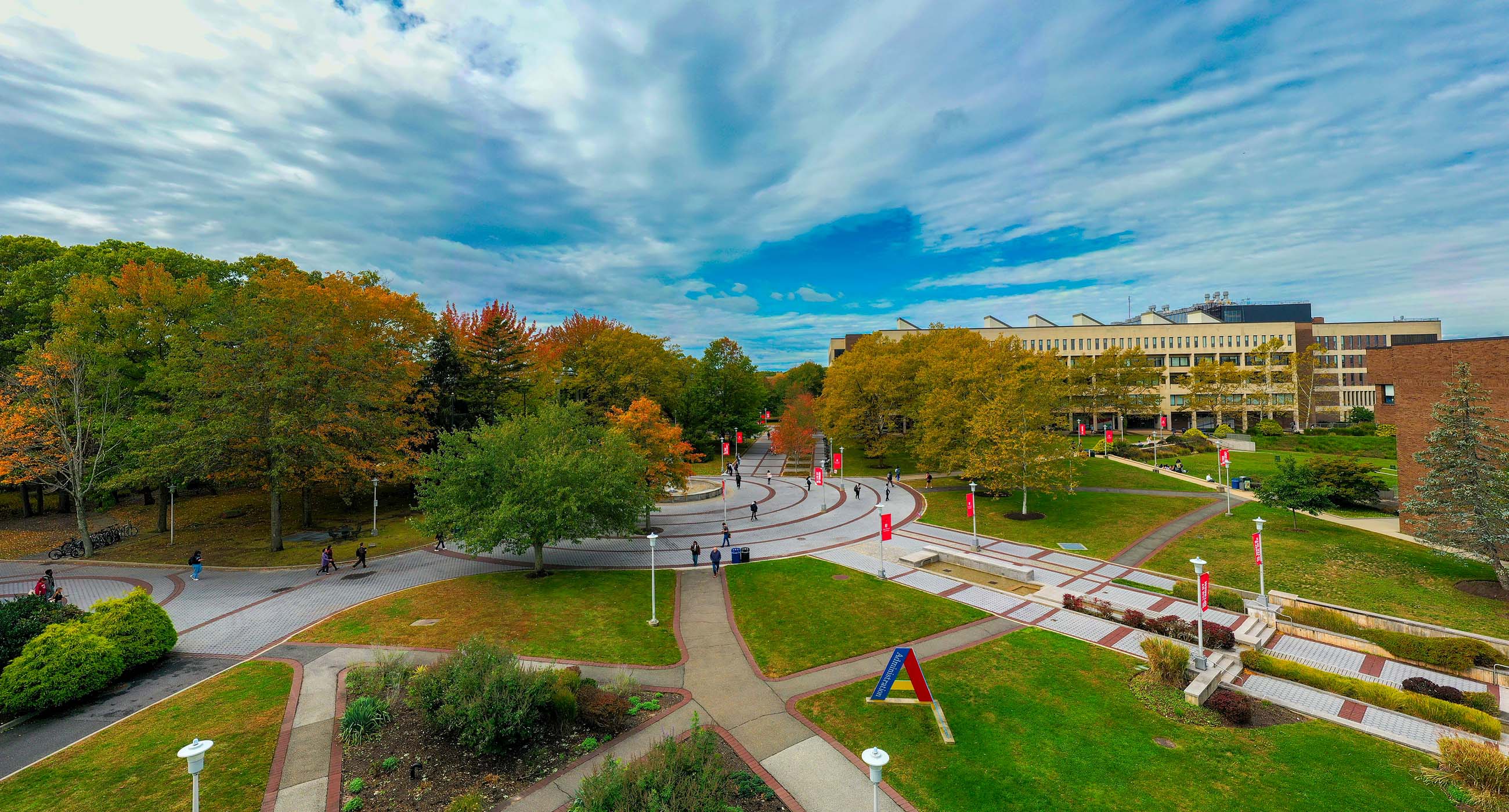 Drone shot of campus from the administration building. People walk on sidewalks under a blue sky.