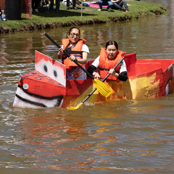 Students floating on Roth Pond in a handmade boat made from painted cardboard and duct tape at the Roth Regatta event