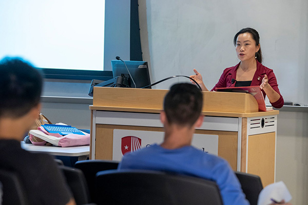 Professor speaking at a podium with two students sitting in the classroom