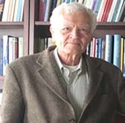 Faculty member standing beside a bookcase.