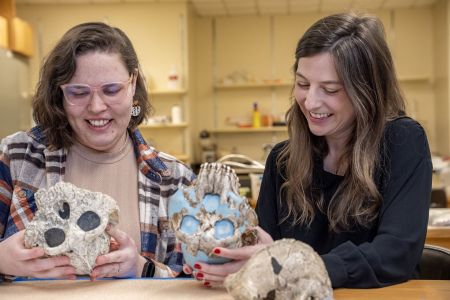 Two anthropologists enthusiastically comparing hominid skull casts within a lab environment
