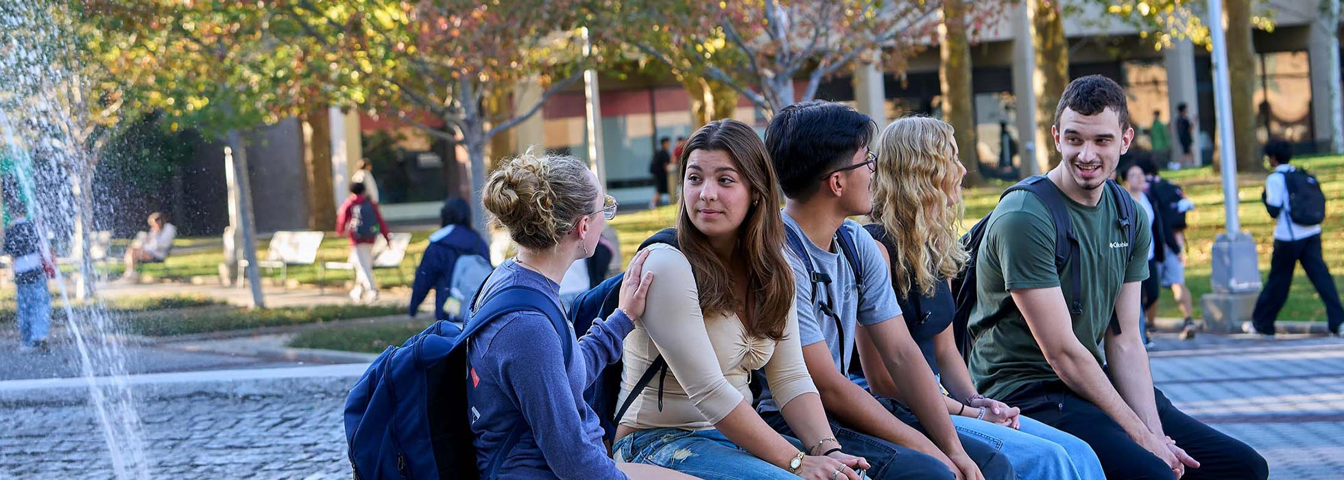 Sitting beside the university fountain, students are chatting and smiling.