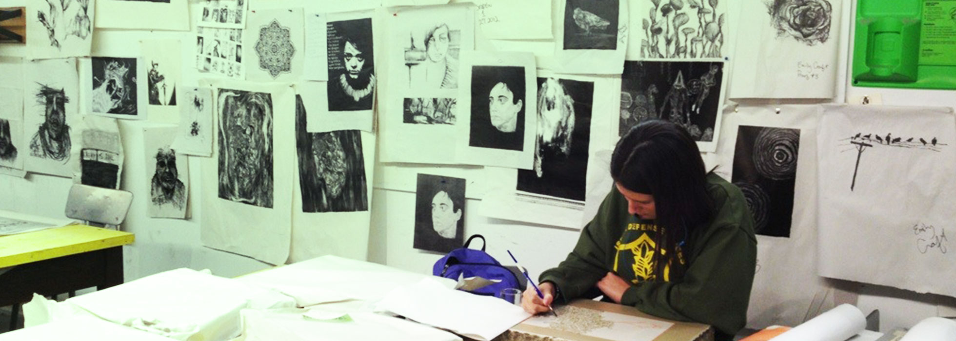 A student at work in a printmaking studio. There are many prints hanging behind the wall