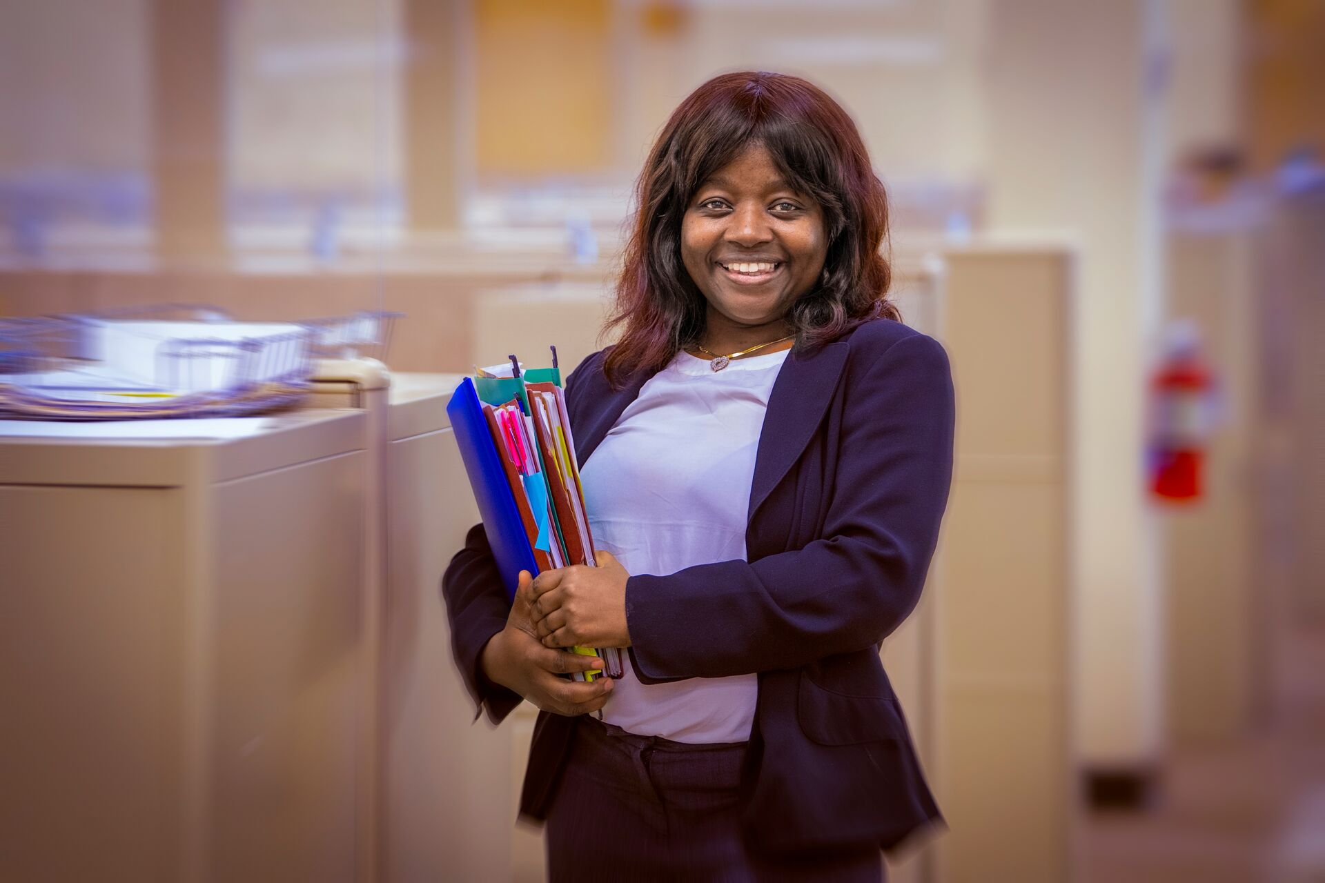 African American woman with bangs and mid-length brown hair, wearing a navy suit, and holding files in her hands