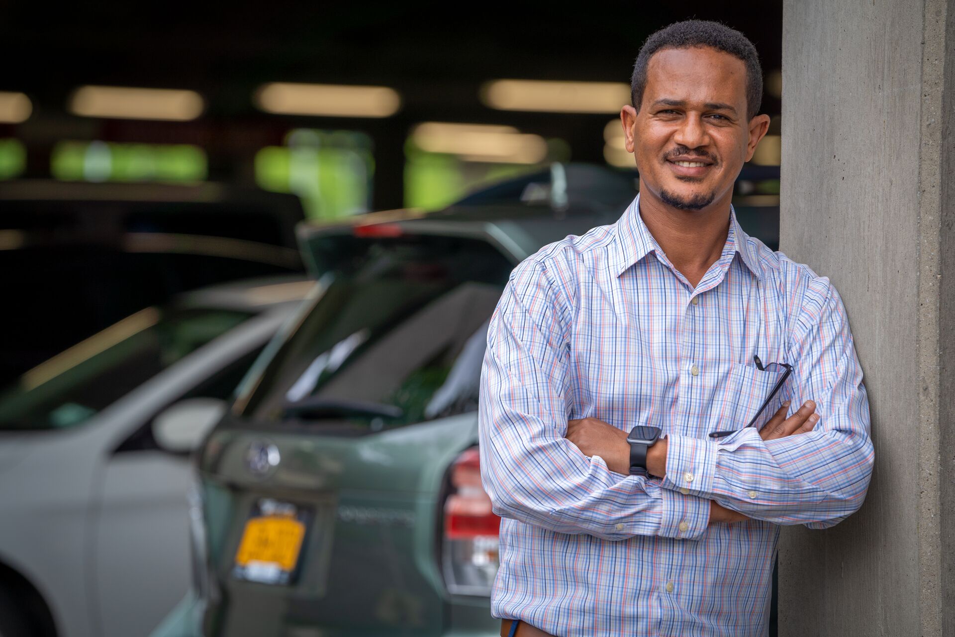 African American man with blue checked button down shirt standing in front of a parking garage