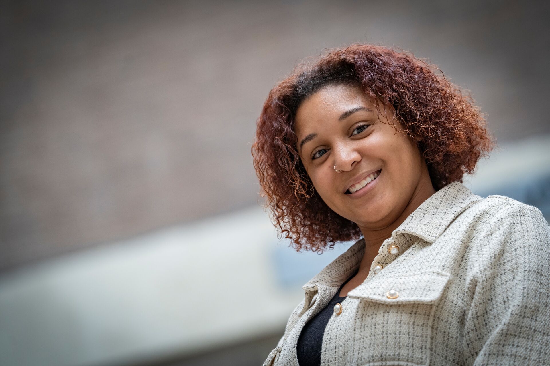 Hispanic woman with short curly auburn hair, wearing tweed jacket with pearl buttons