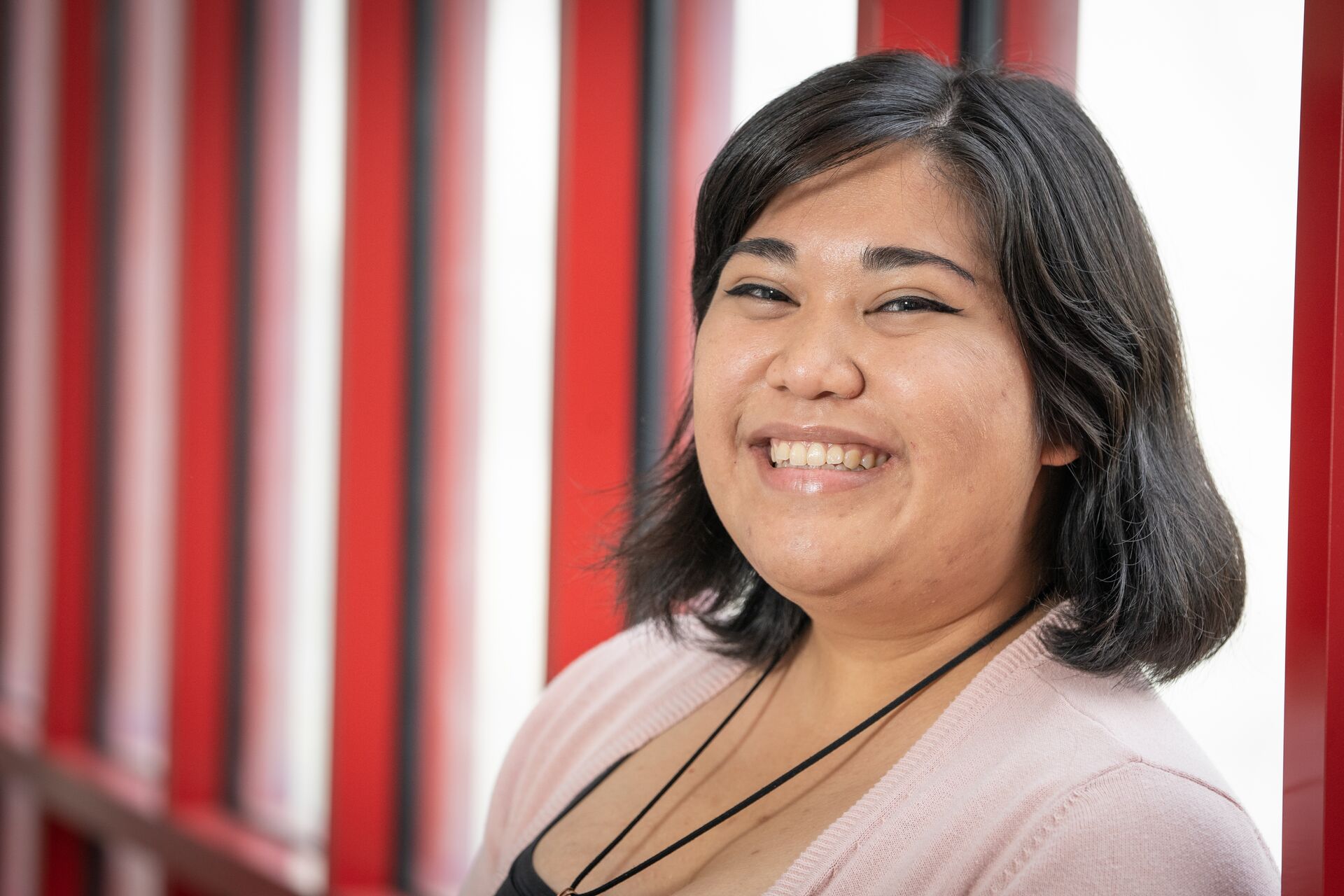 Hispanic woman with short brown hair, wearing a pink cardigan over a black shirt with a black cord necklace