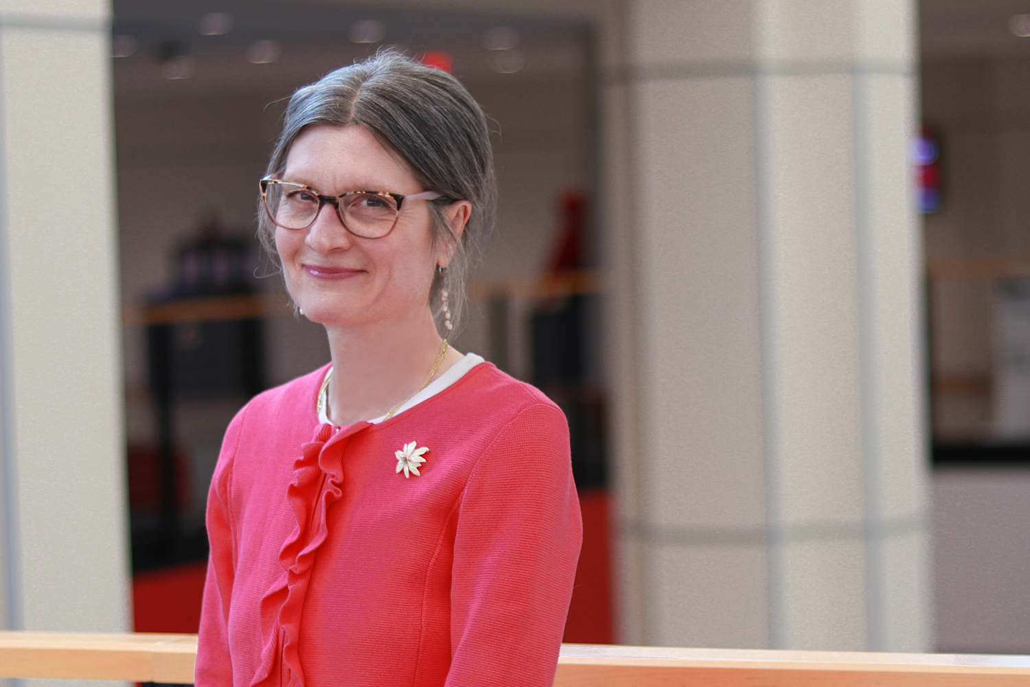 White woman with hair tied back and glasses (Catherine), smiling and wearing a pink sweater (