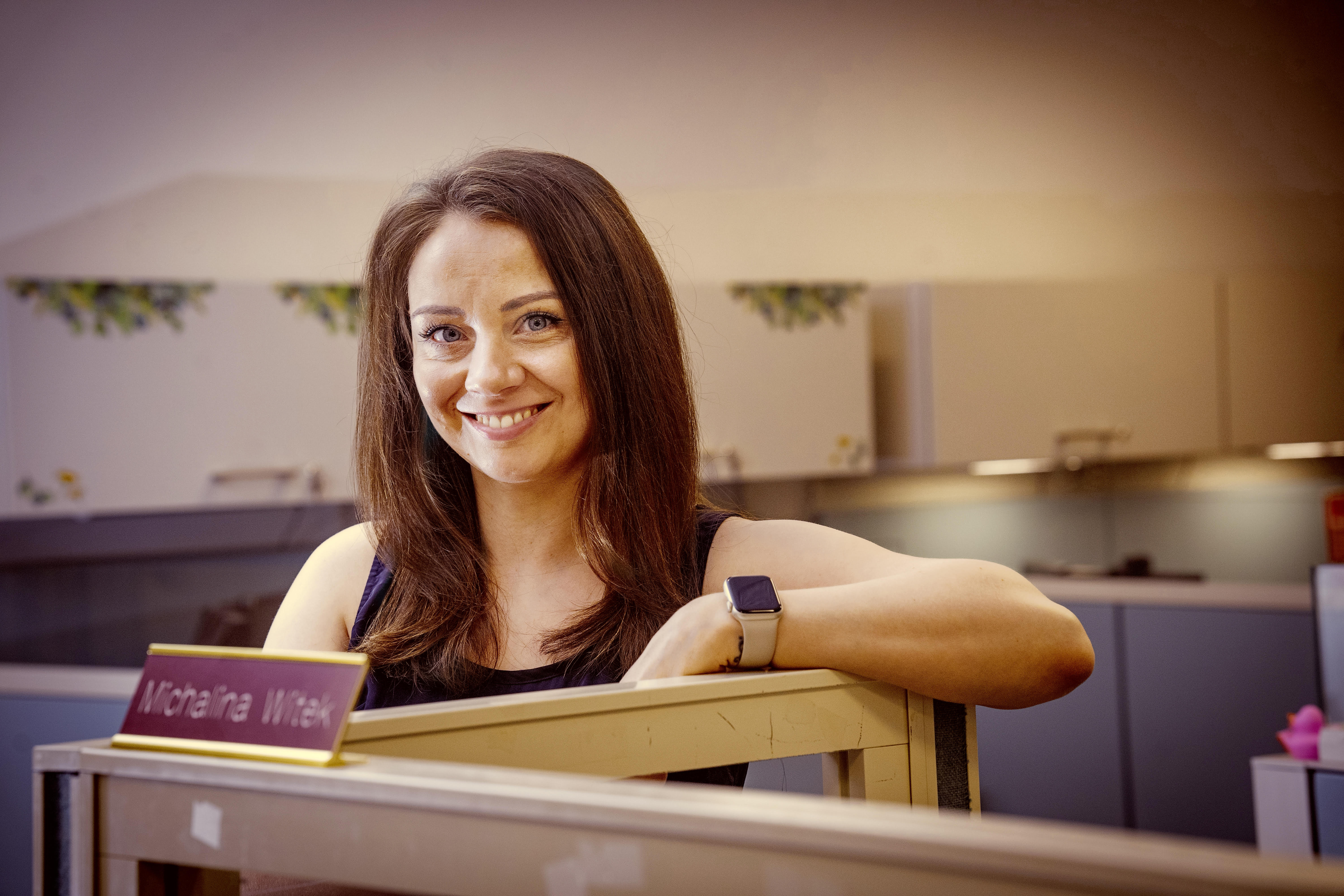 Brunette caucasian woman wearing black tank top and watch, standing behind cubicle