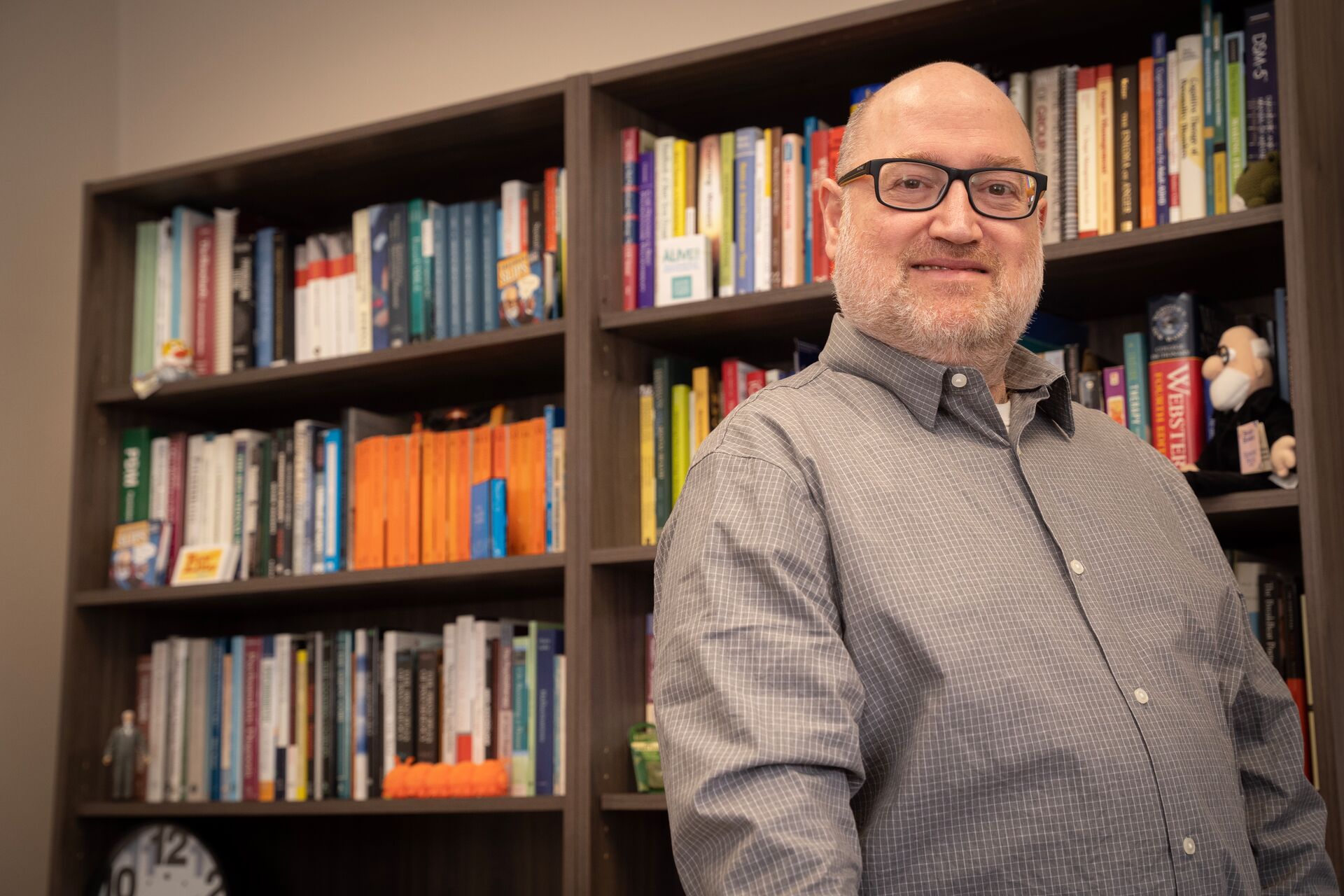 Caucasian man wearing glasses and button down, standing against bookshelf