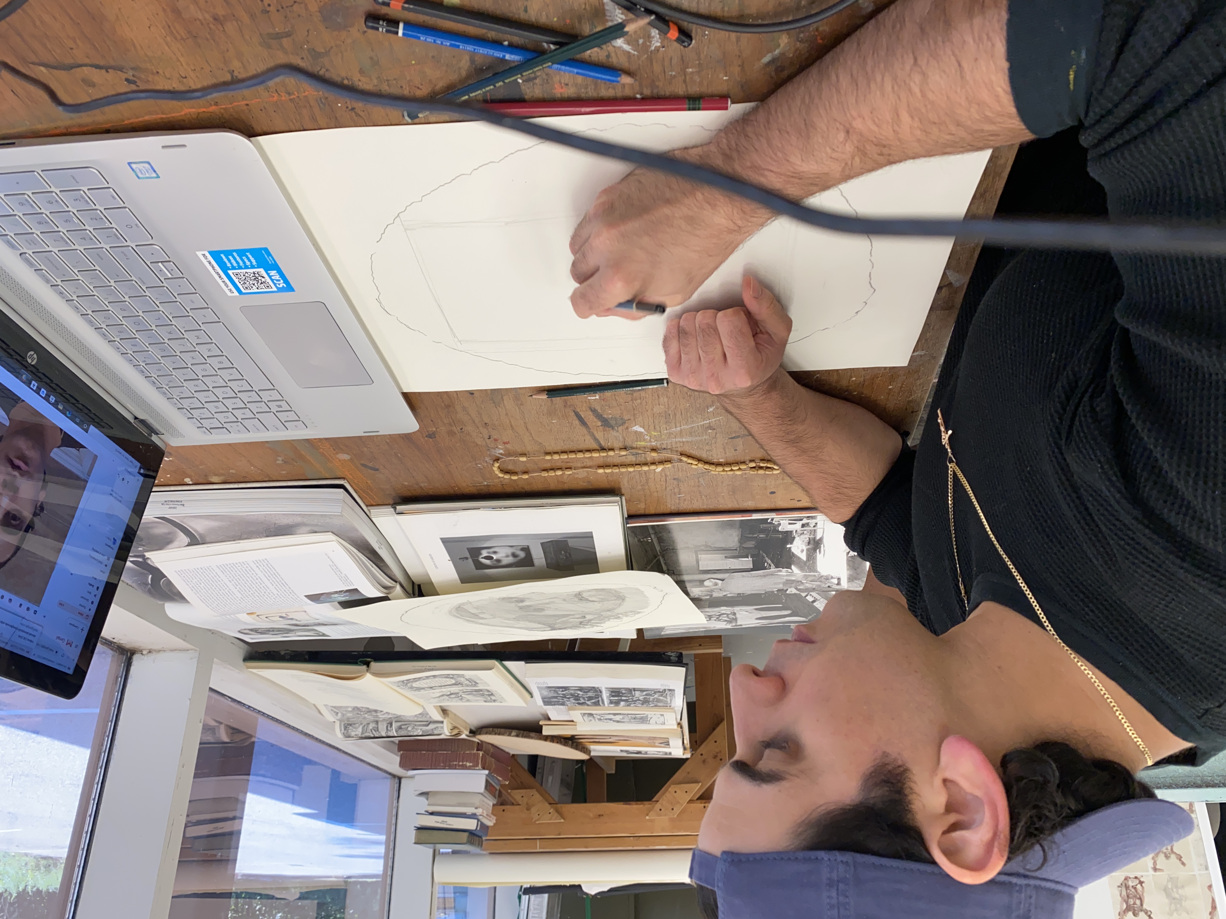 Man wearing blue baseball cap sketching in front of a laptop
