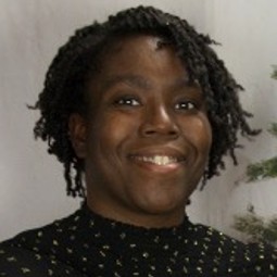 African American woman with short locked/curled hair, black shirt with white polka dots