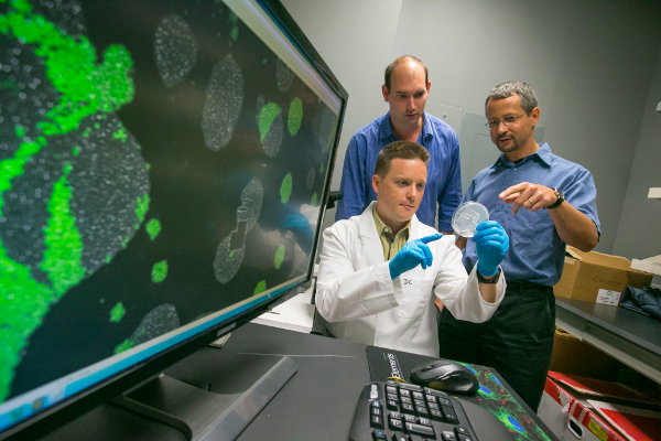 Dr. Balaszi and his team looking at a petri dish next to a copmuter screen