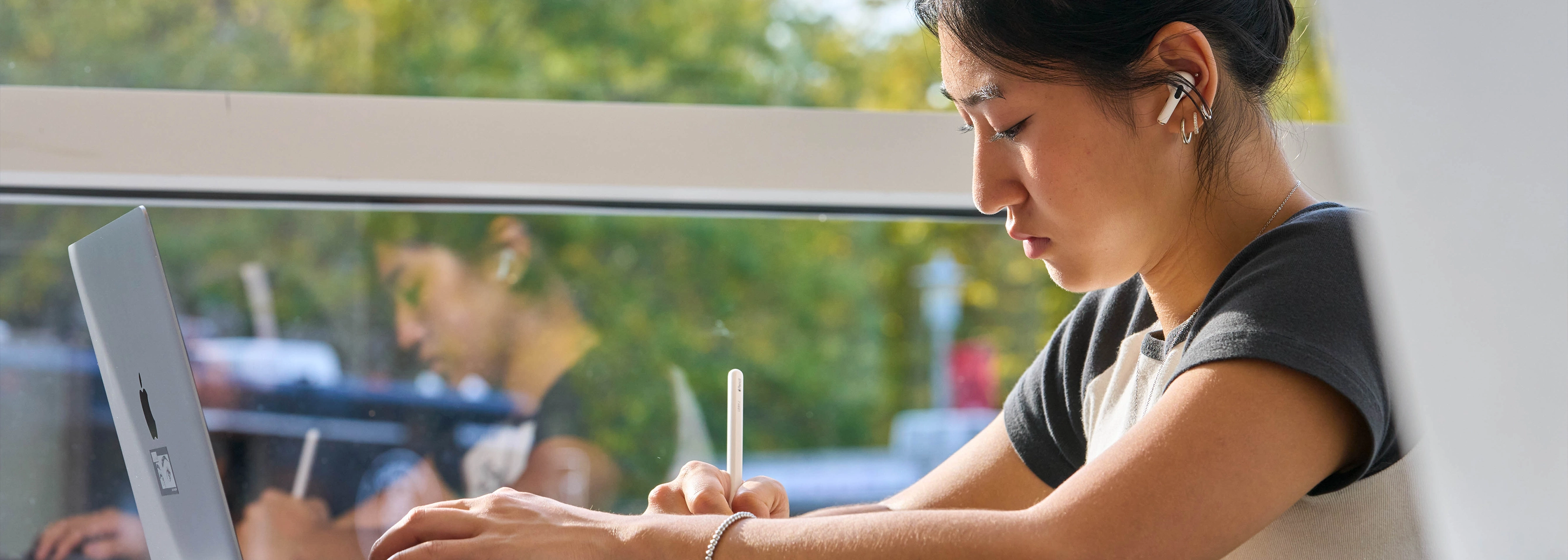 Person writing with a stylus on a laptop at a desk near a window