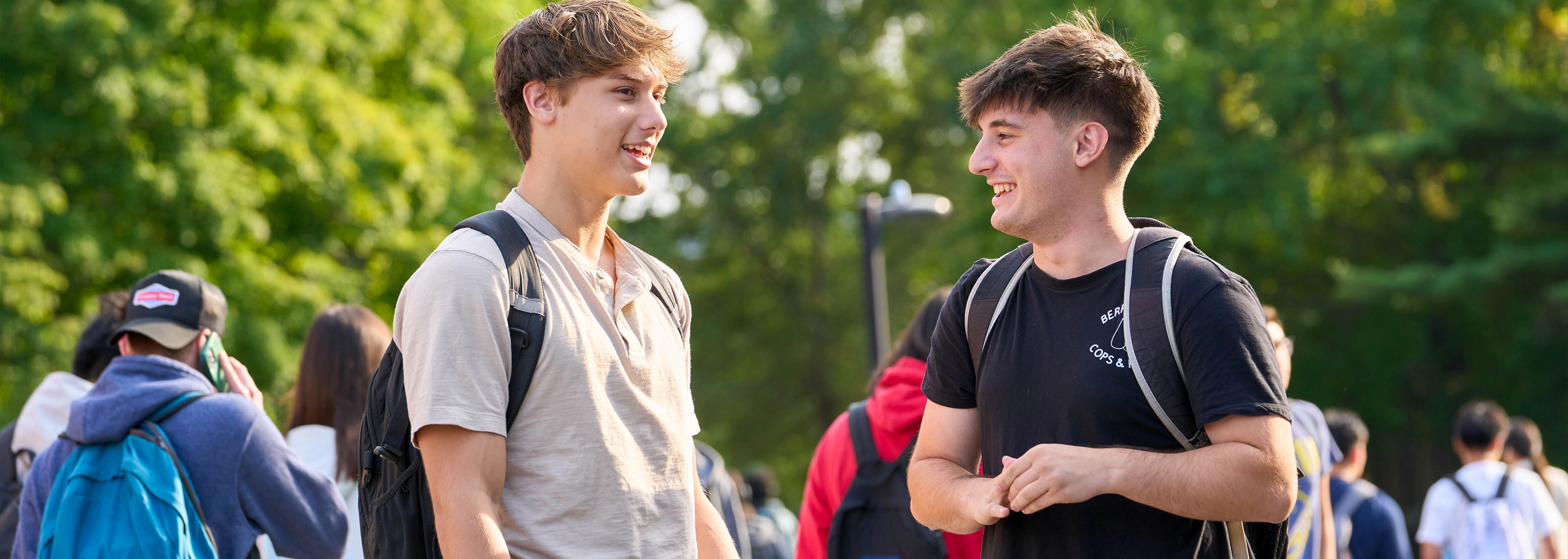 Two college students with backpacks talking and smiling outdoors on the Stony Brook University campus