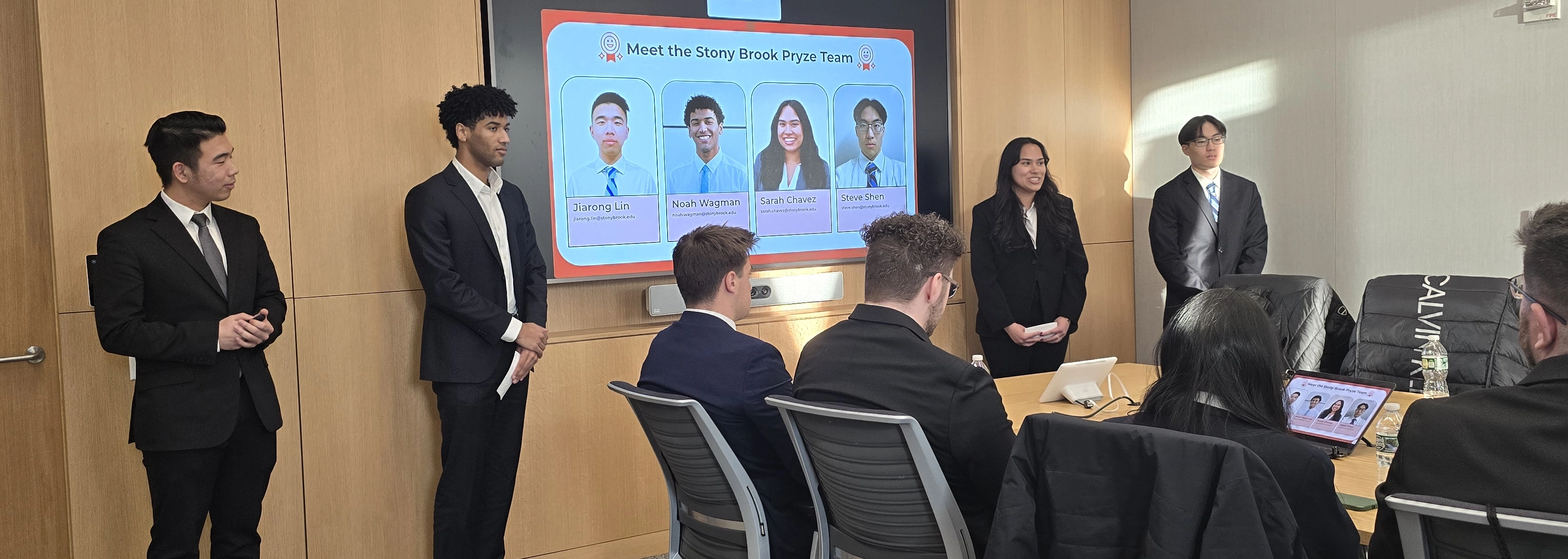 College of Business students in professional attire presenting the Stony Brook Pryze Team to a seated panel in a conference room