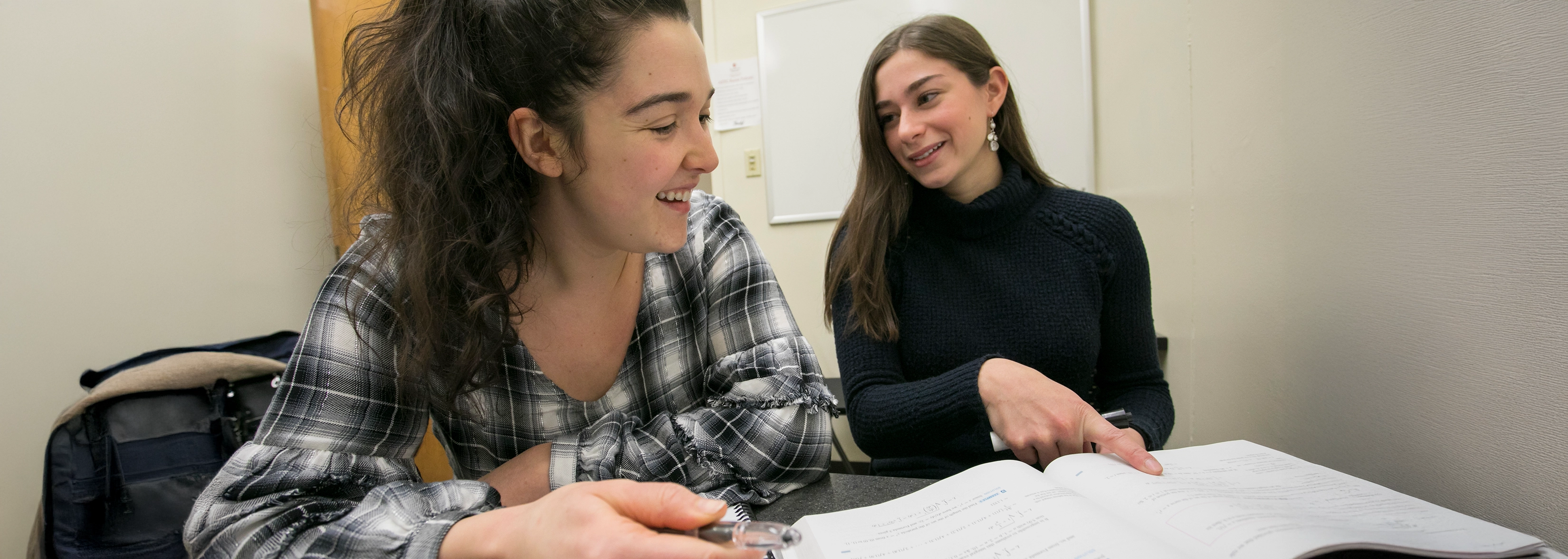 Two people studying at a table, smiling and discussing an open book