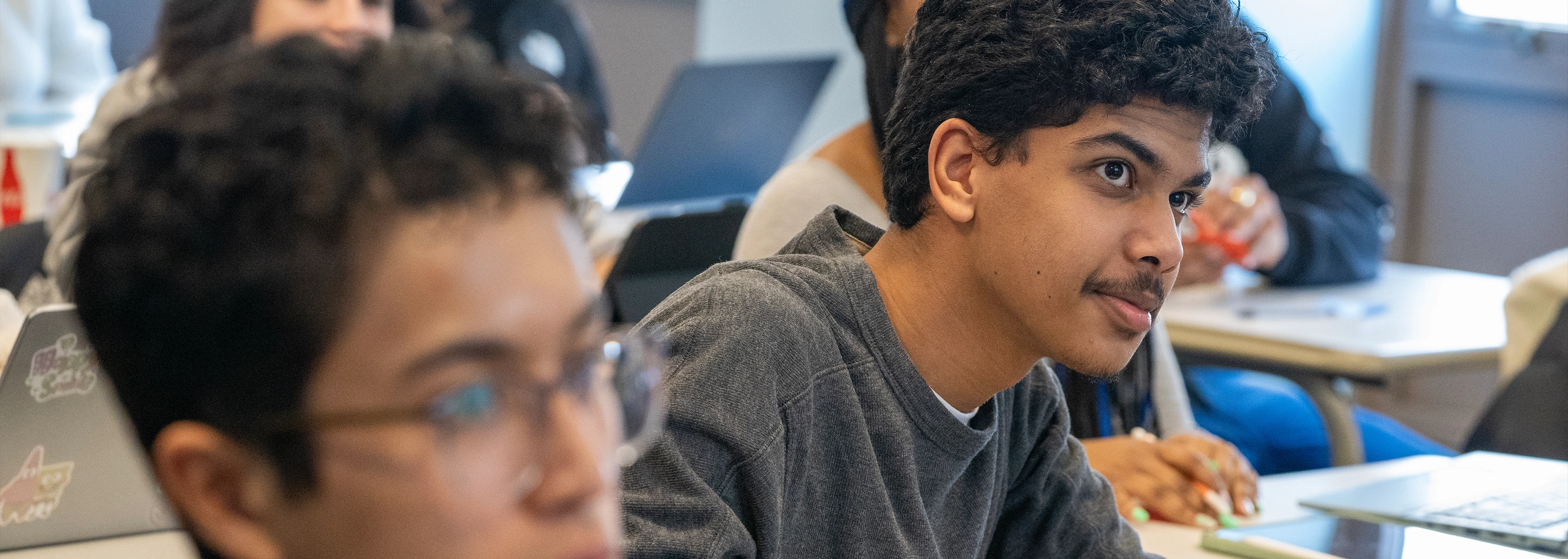 A student in a classroom, focused and holding a pen