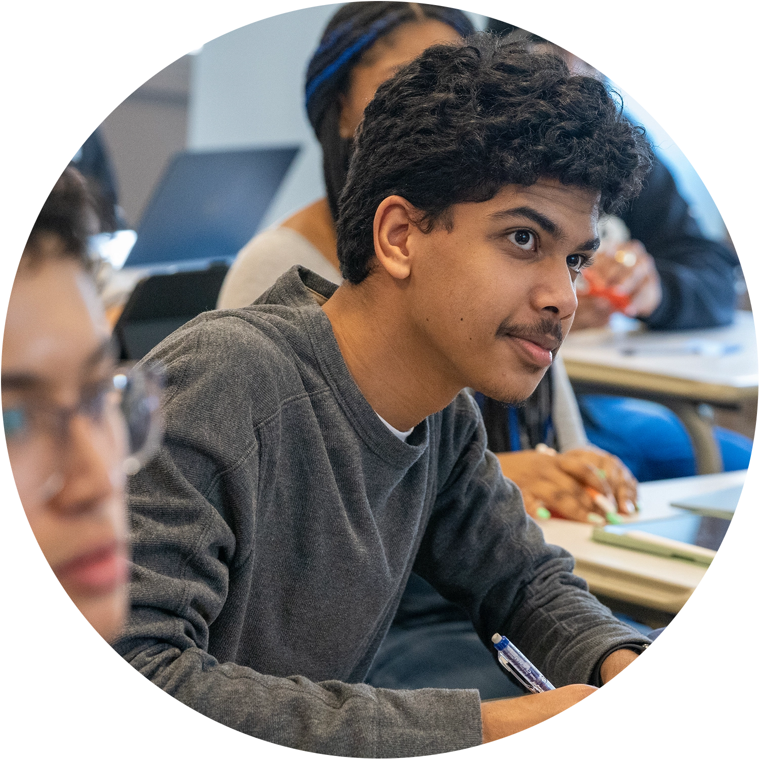 A student in a classroom, focused and holding a pen