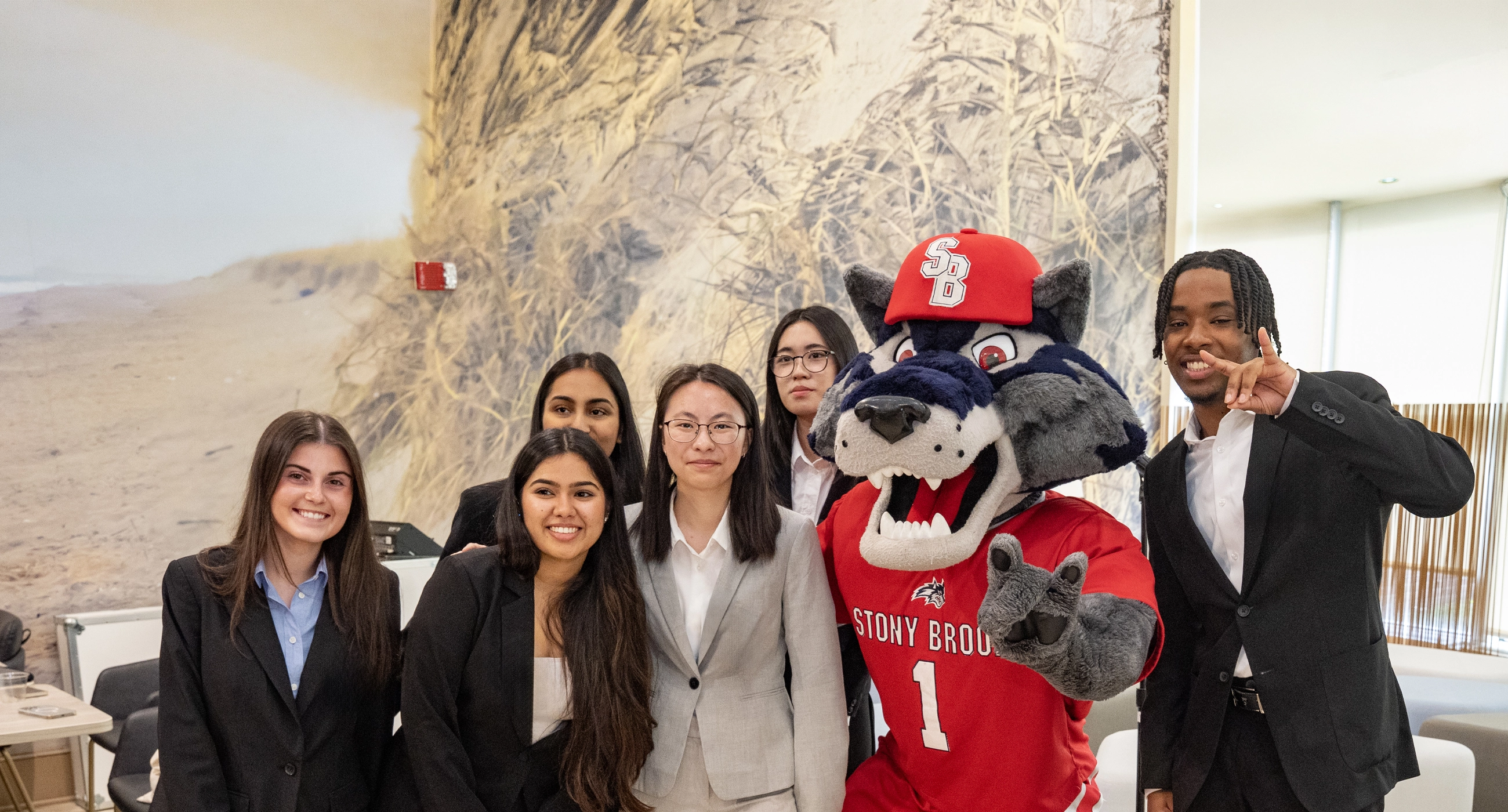A group of five people in formal attire poses with a mascot in a red uniform indoors.