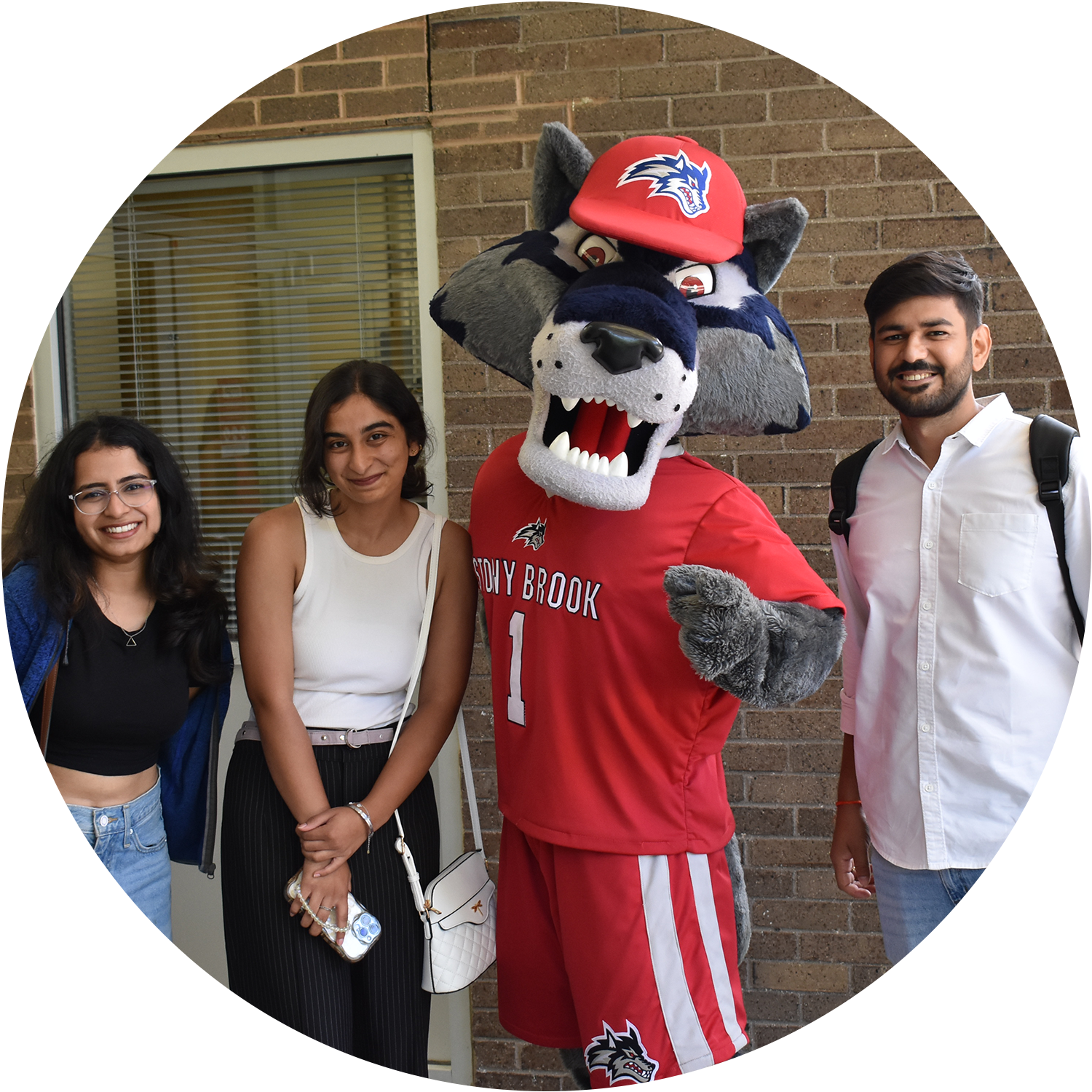 Three people pose with a wolf mascot in a red uniform labeled "STONY BROOK."