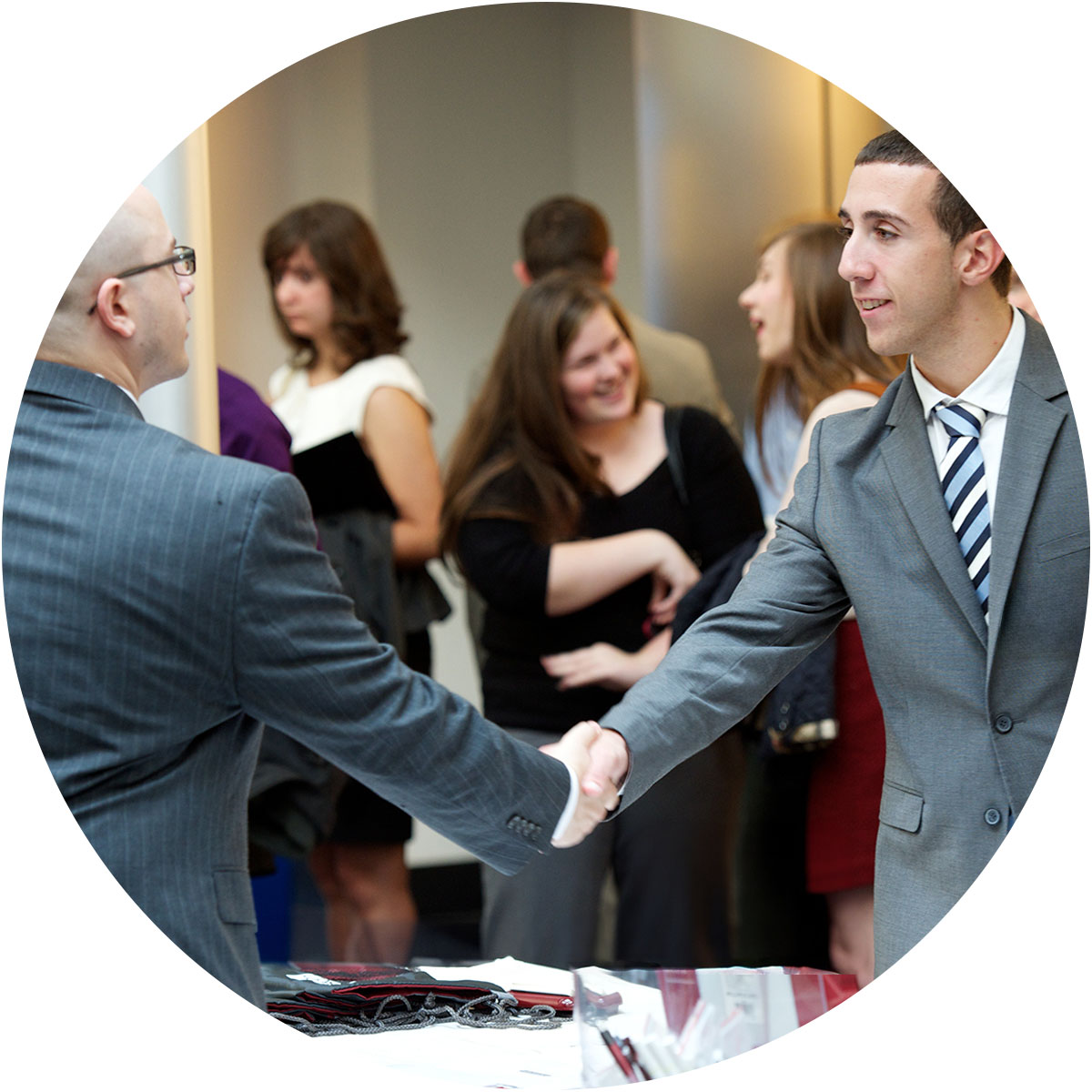 Two men in suits shaking hands at a formal event with people conversing in the background