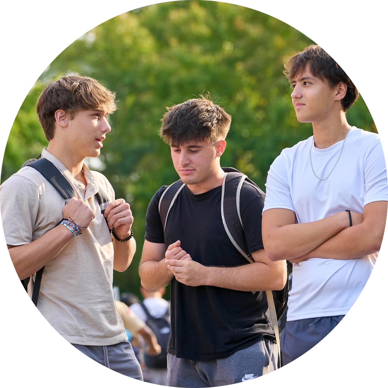 Three young men talking outdoors with a green background