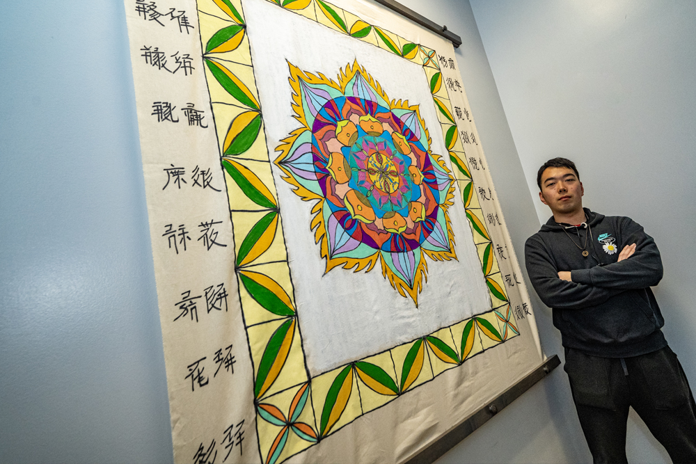 student standing next to painted and hanging mandala