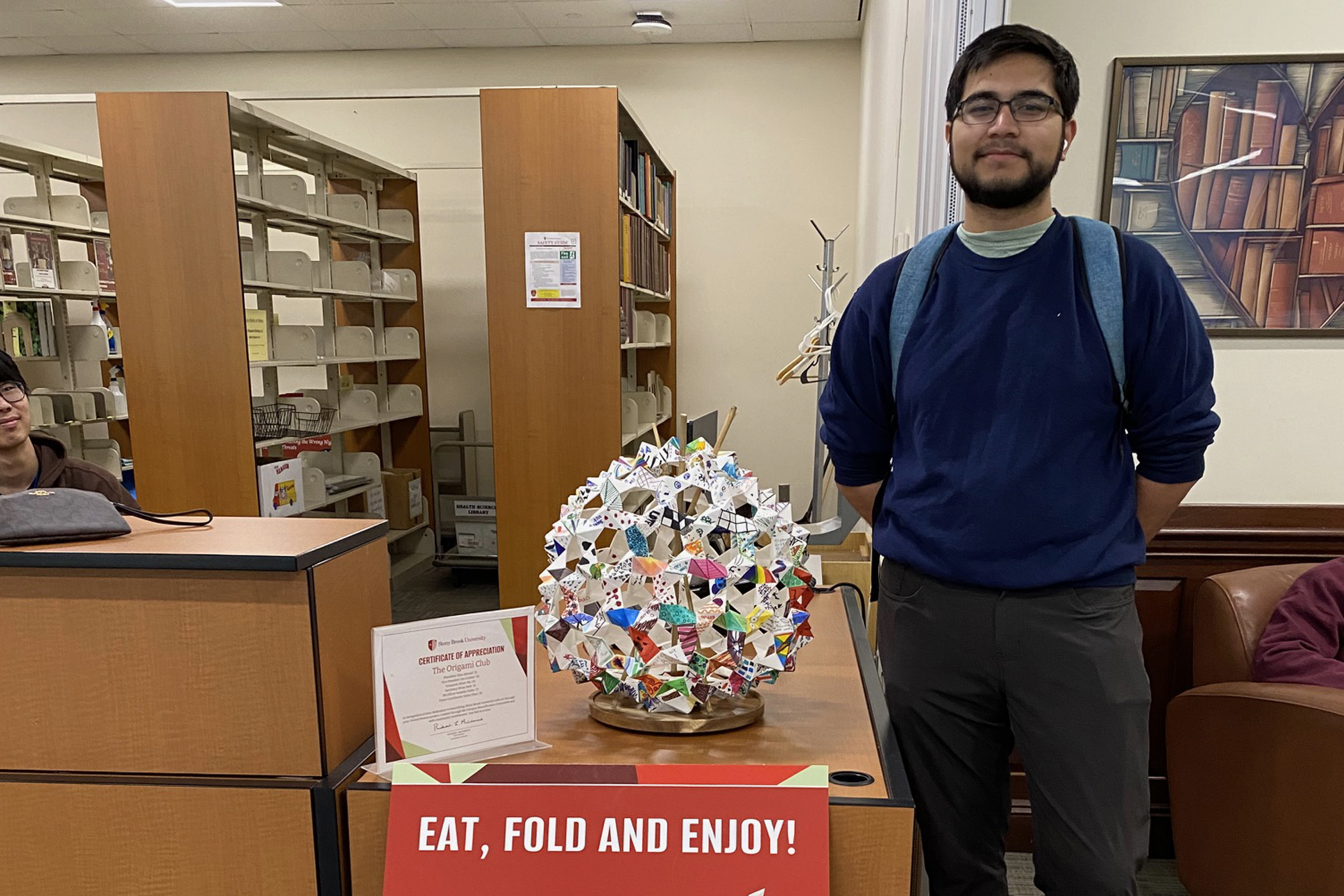 student standing next to circular origami project on a wooden desk