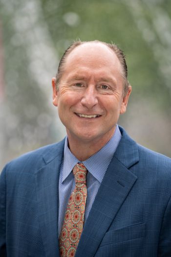 David Wrobel, wearing a blue suit, striped light blue shirt and patterned orange tie.