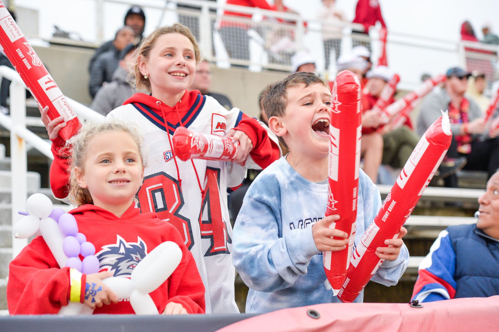 Three children wearing Stony Brook Gear cheer in the stands