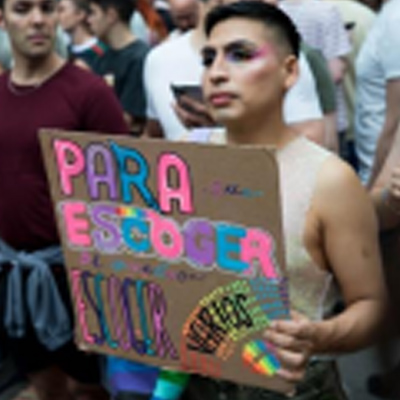 Person at a Pride parade holding a sign that reads "PARA ESCOGER AMAR.